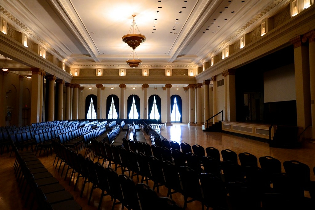 Large ballroom with rows of empty black chairs and a stage.